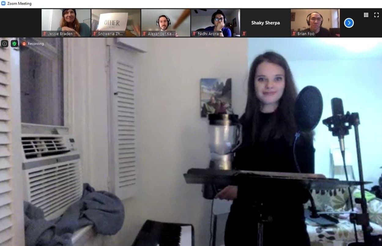 A singer performing in a home studio on a Zoom call, with participants in thumbnails above
